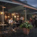 Eine Zwischen zwei Sonnenschirmen gespannte Regenrinne über einer Gastro-Terrasse