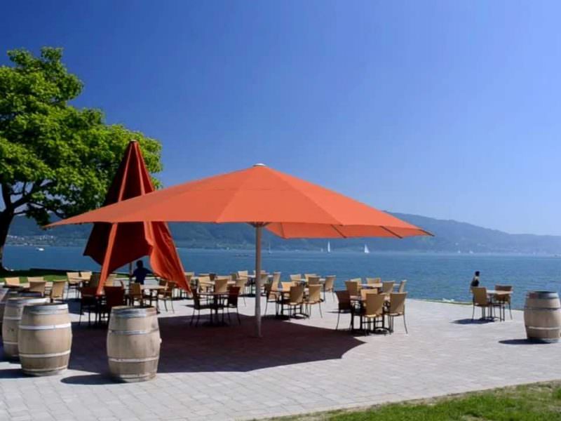 Zwei Orange Sonnenschirme auf einer Terrasse vor einem See.