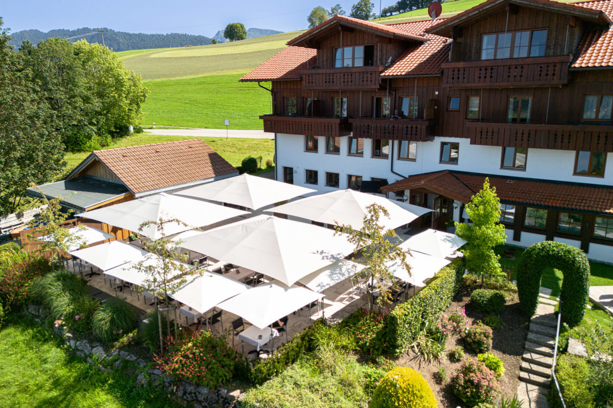 Ansicht der Terrasse des Birkenhof in Steibis mit großen und etwas kleineren weißen Sonnenschirmen.
